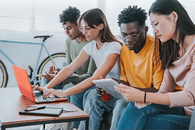 a group of students crowded around a laptop solving a problem