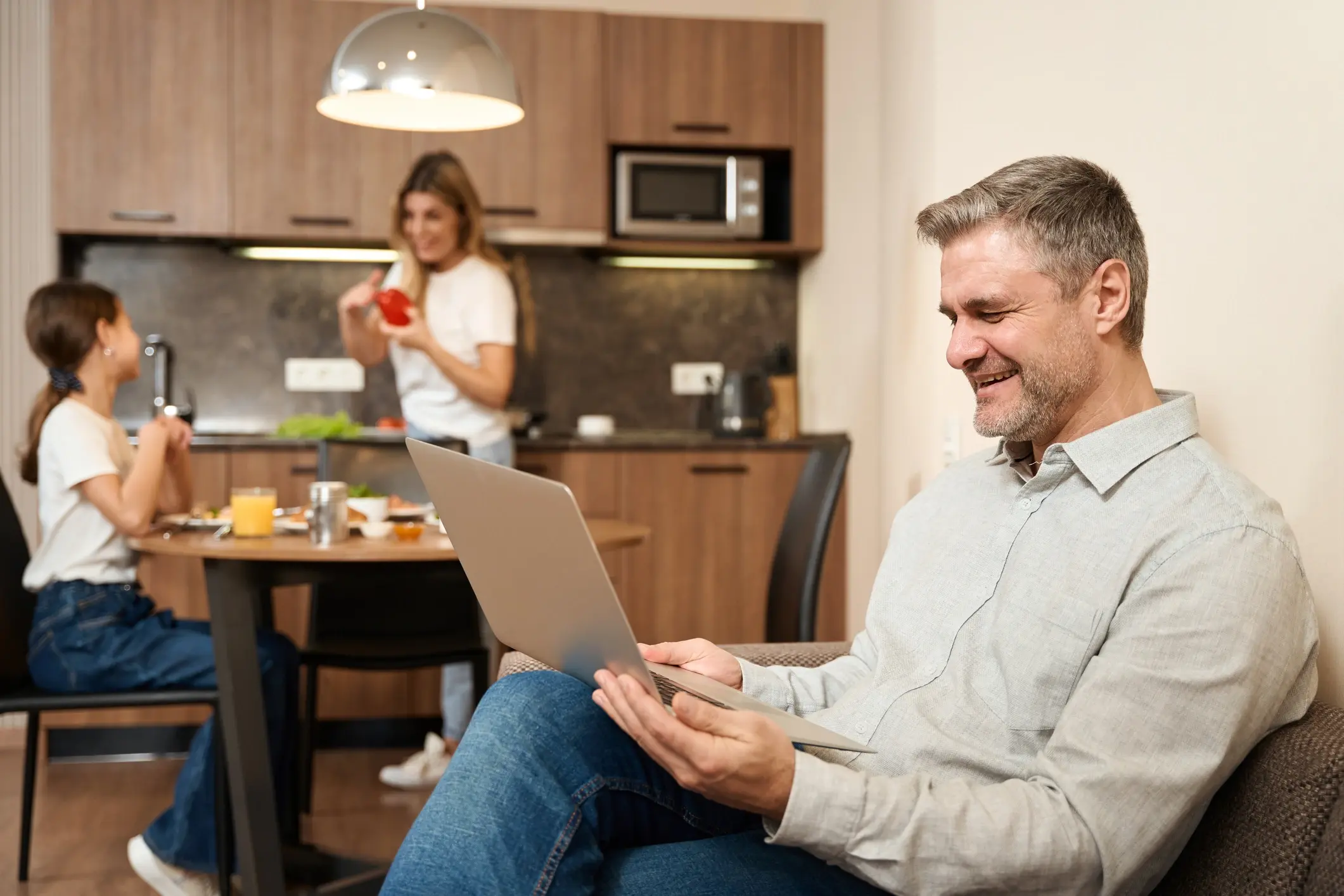 happy looking man working on his laptop while his family are in the background