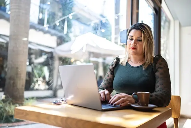 a woman sat by a window on her laptop in a cafe