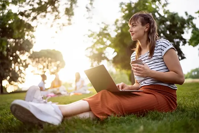 woman sitting on the grass in a park with a laptop